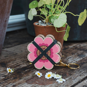 Floral keychain with a pink flower design on a wooden surface with flowers around