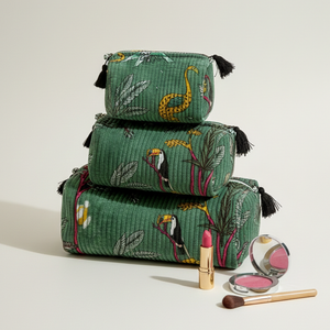 Three stacked green makeup pouches with a tropical bird and leaf pattern, styled with cosmetic items on a light beige background.