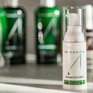 Dr. Alkaitis organic eye crème bottle on a shelf with green and white bottles in the background.