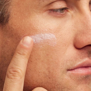 Close-up of a man applying cream to his face with his finger.