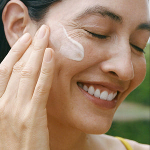 Woman applying cream to her face with a blurred natural background