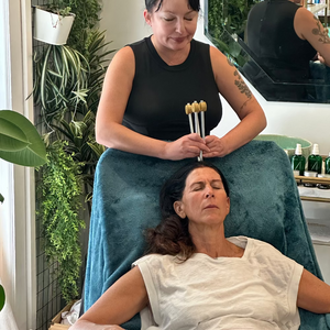 Woman receiving a head massage from another woman using tuning forks in a spa setting.