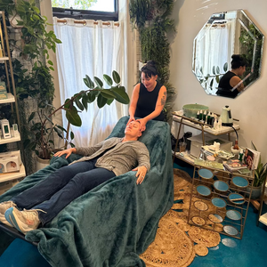 Person receiving a facial massage in a spa-like setting with plants and mirrors at Wildcraft Charleston.