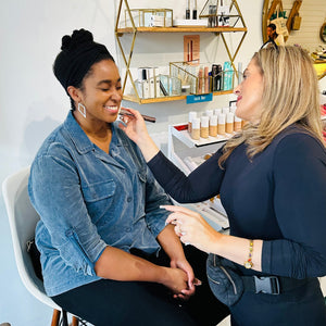 Woman getting makeup applied by another woman in a beauty salon setting.