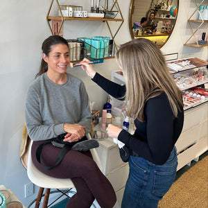 Two people in a room with one having makeup applied by a makeup artist