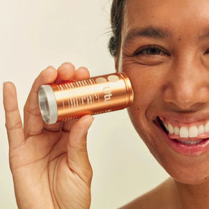 Person holding a rose gold compact mirror close to their face against a neutral background