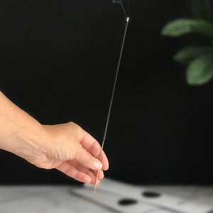 Hand holding a lit incense stick with smoke against a dark background