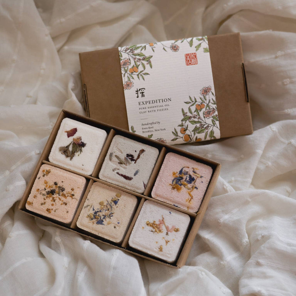 Set of six small square items in a box with a decorative label on a white fabric background