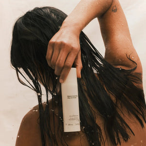 Person with wet hair holding a white bottle against a neutral background