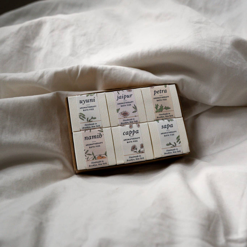 Set of six small square items in a box with a decorative label on a white fabric background