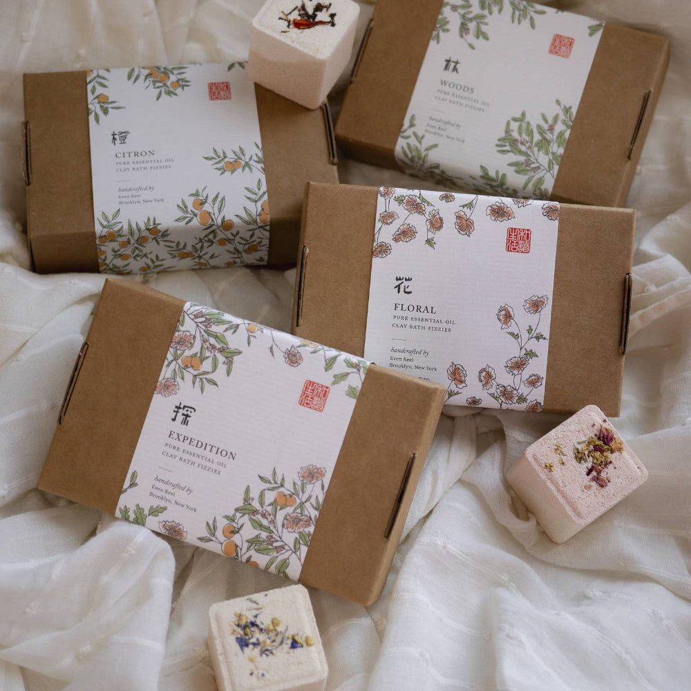 Various soap bars in brown boxes with decorative labels on a white fabric background