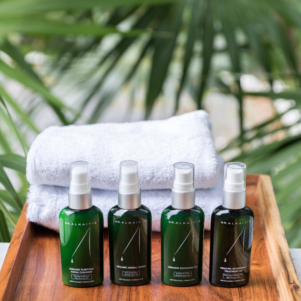 Four green bottles with silver caps on a wooden tray with a white towel, against a blurred green leafy background.