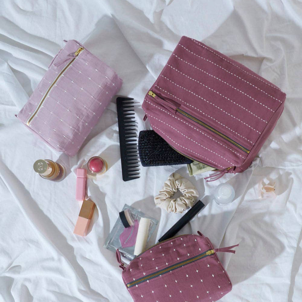 Pink toiletry bags with travel items on a white bedspread