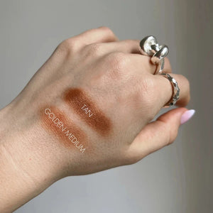 Hand with three different makeup swatches labeled 'Tan', 'Medium', and 'Golden Medium' on a neutral background.