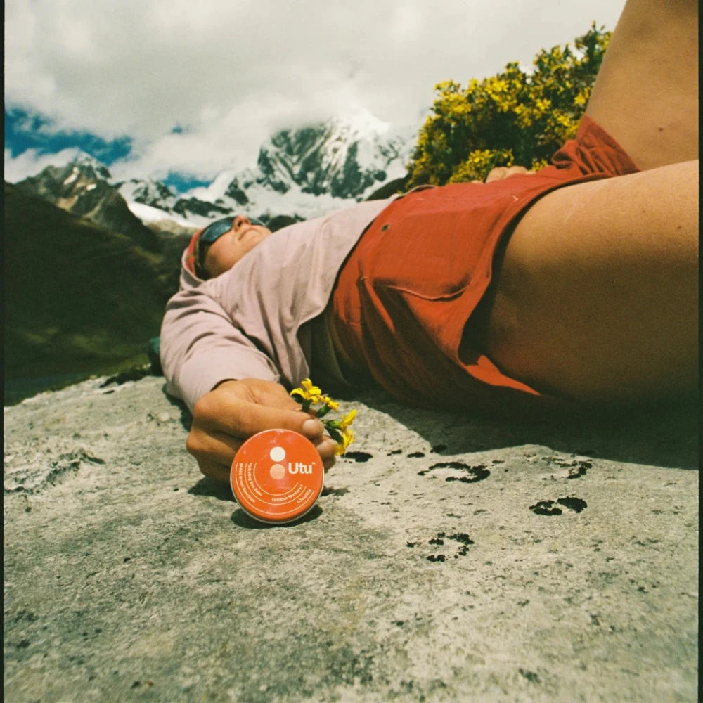 Person lying on a rock with a scenic mountain background, holding a bottle labeled 'Ultima'.