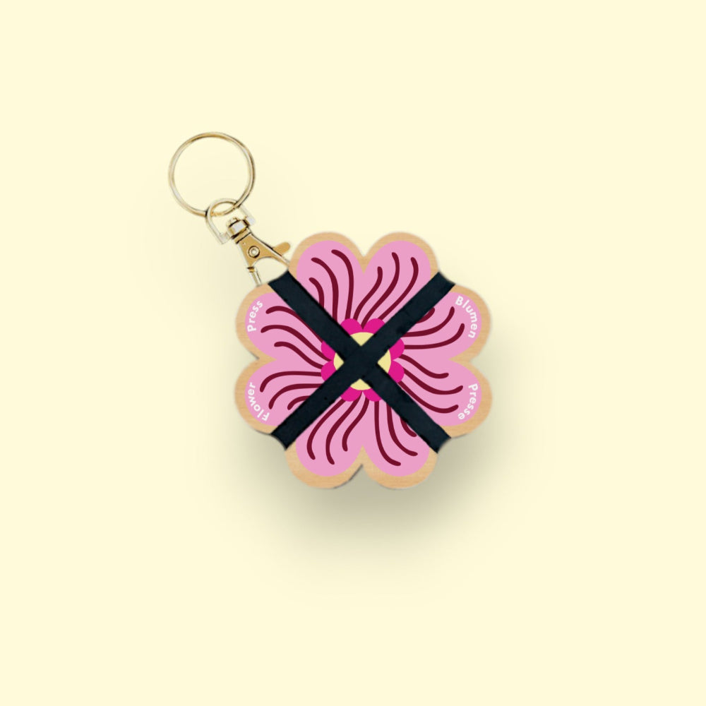 Keychain with pink floral design and black ribbon on a beige background