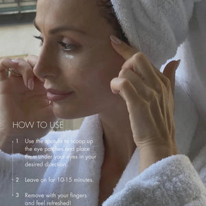 Woman applying eye patches with a towel on her head, surrounded by eye patches.