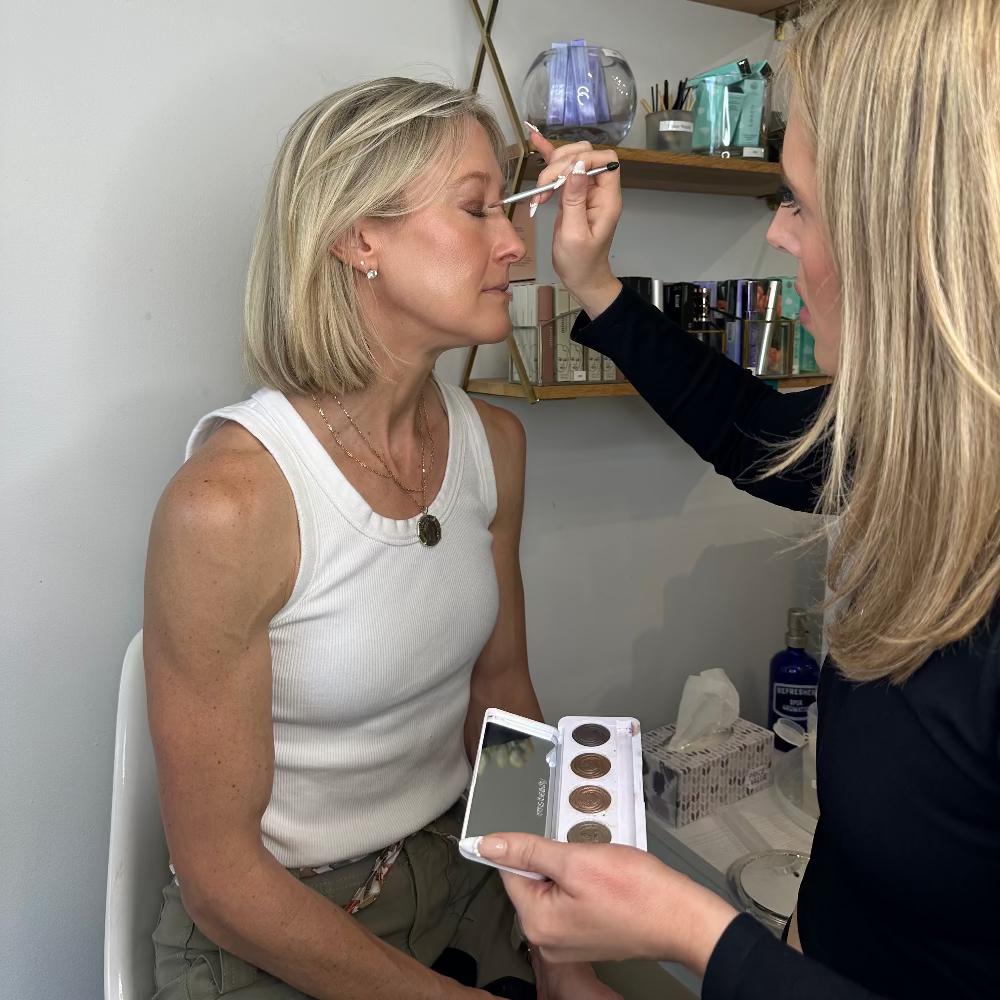 Makeup artist applying makeup to a client in a home setting.