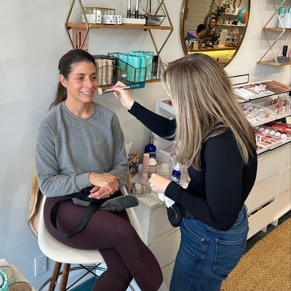 Two people in a room with one having makeup applied by a makeup artist