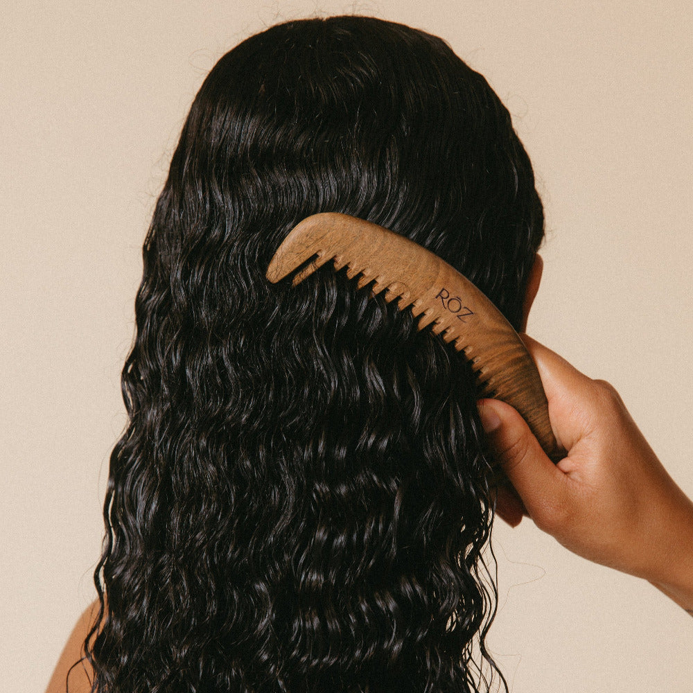 Person combing long, wavy hair with a wooden comb on a beige background