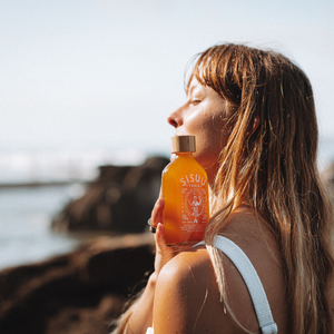Woman holding an orange bottle labeled 'Sisu' by a body of water