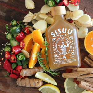 SISUU Tonic bottle surrounded by fruits, vegetables, and herbs on a wooden surface
