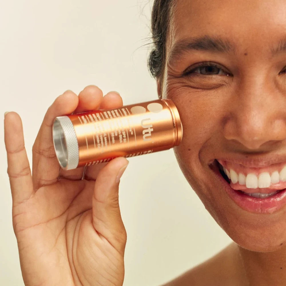 Person holding a rose gold compact mirror close to their face against a neutral background