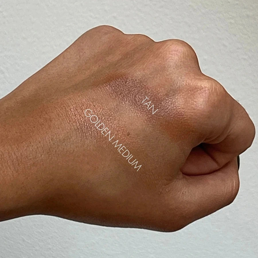 Hand swatching makeup on a white background with 'TAN' and 'GOLDEN MEDIUM' labels.