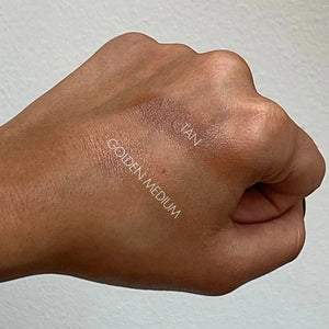 Hand swatching makeup on a white background with 'TAN' and 'GOLDEN MEDIUM' labels.