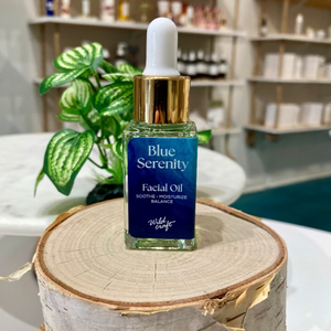 Facial oil bottle labeled 'Blue Serenity' on a wooden block with a blurred background