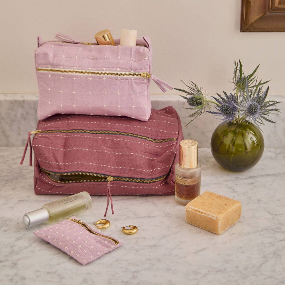 Pink and purple cosmetic bags with toiletries on a marble surface.