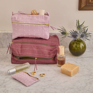 Pink and purple cosmetic bags with toiletries on a marble surface.