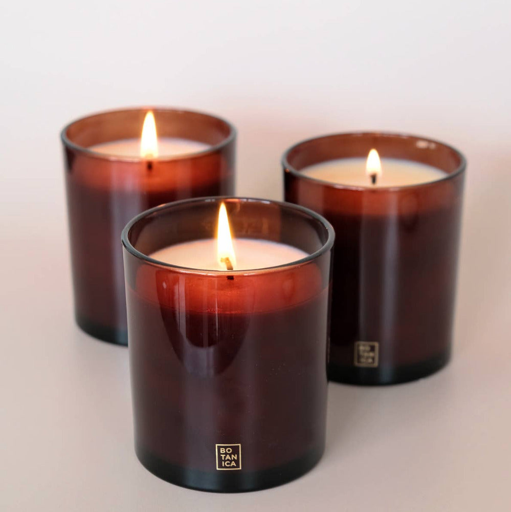 Three lit candles in brown glass containers on a light background