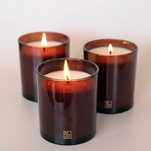 Three lit candles in brown glass containers on a light background