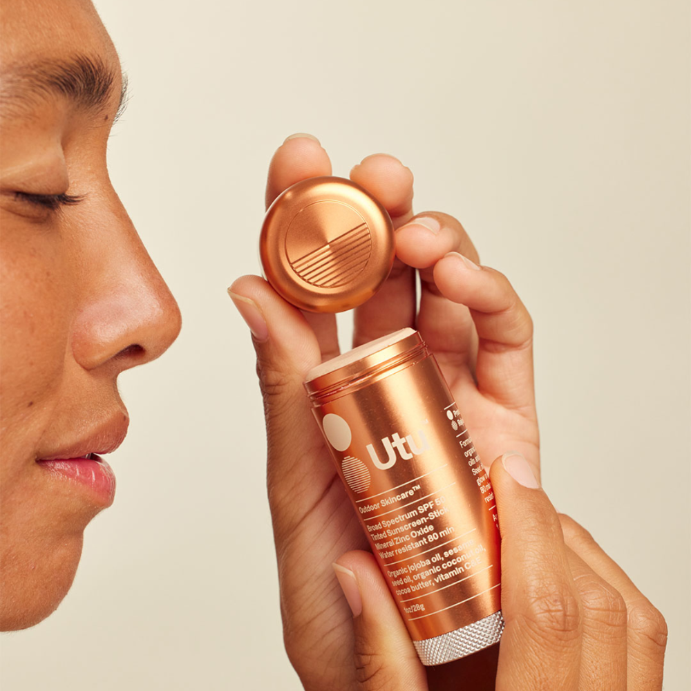 Person using a bronze-colored skincare device on their face against a beige background